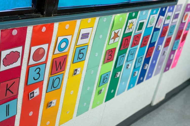 Colorful task box labels with shapes, letters and numbers on a special education classroom wall
